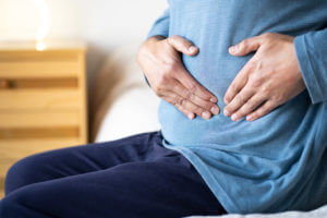 Man sits alone on his bed, suffering from stomach cramps possibly due to Crohn's disease.